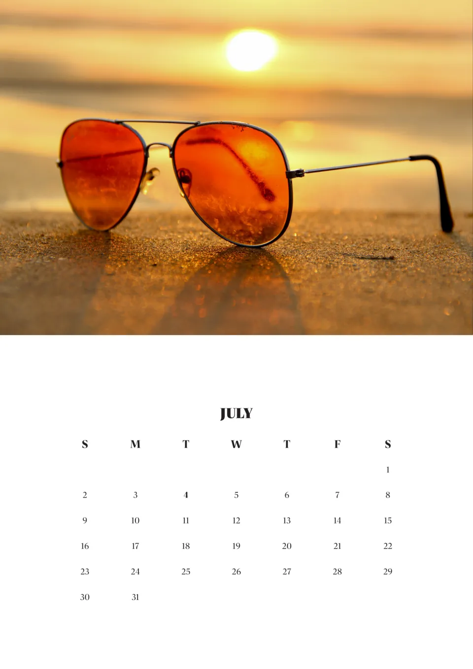July 2023 month page with a photo of orange aviator sunglasses resting on sand at sunset; July 4 shown in bold
