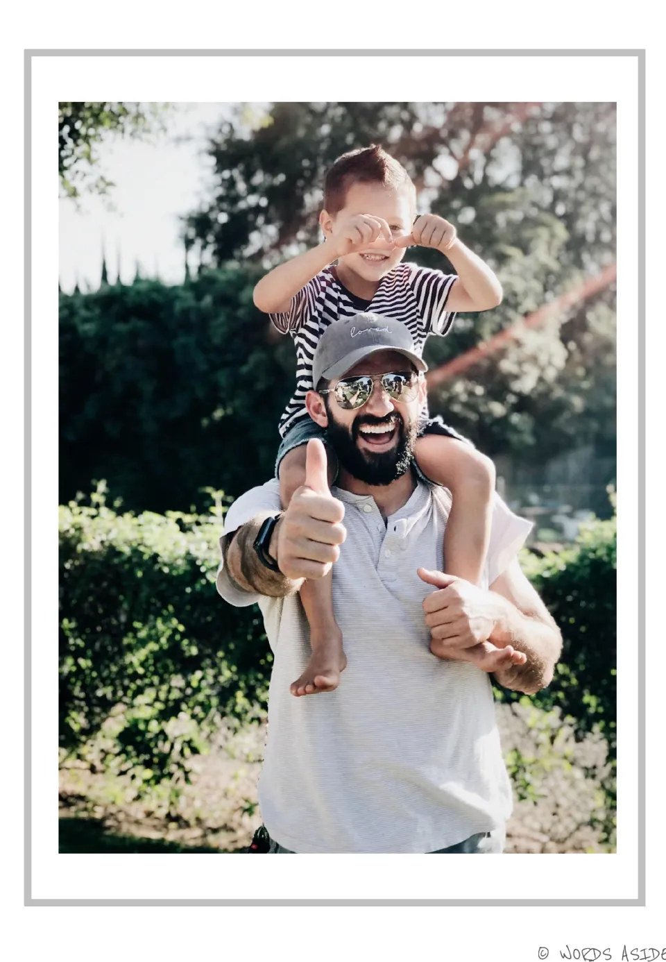 Story reference photograph for AAC picture description: a smiling man carries a child on his shoulders outdoors