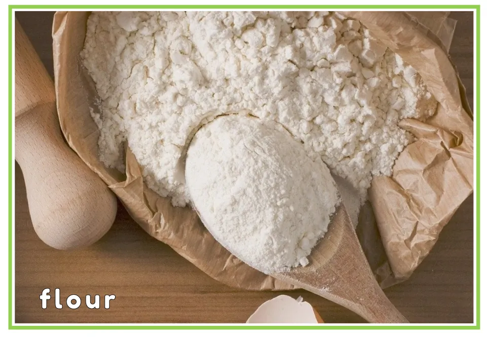 Flour vocabulary card: the printed word flour on a photo of a wooden spoon scooping white flour from a paper bag