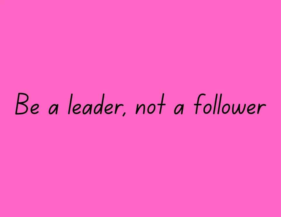 Leadership sign reading "Be a leader, not a follower" in thin black handwriting-style print on a bright pink background