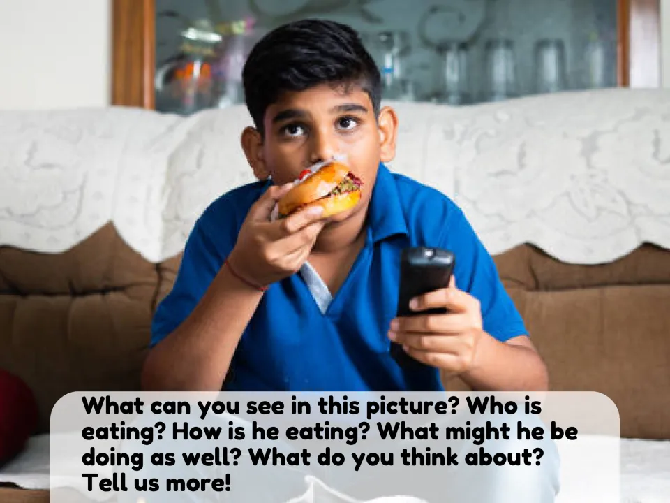 Picture description: a boy eats a burger on a sofa holding a TV remote; students answer who is eating, how and why