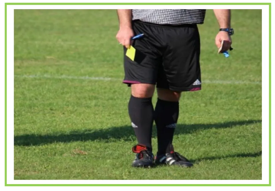 Picture-only soccer vocabulary flashcard for referee, showing an official holding a yellow card on the field