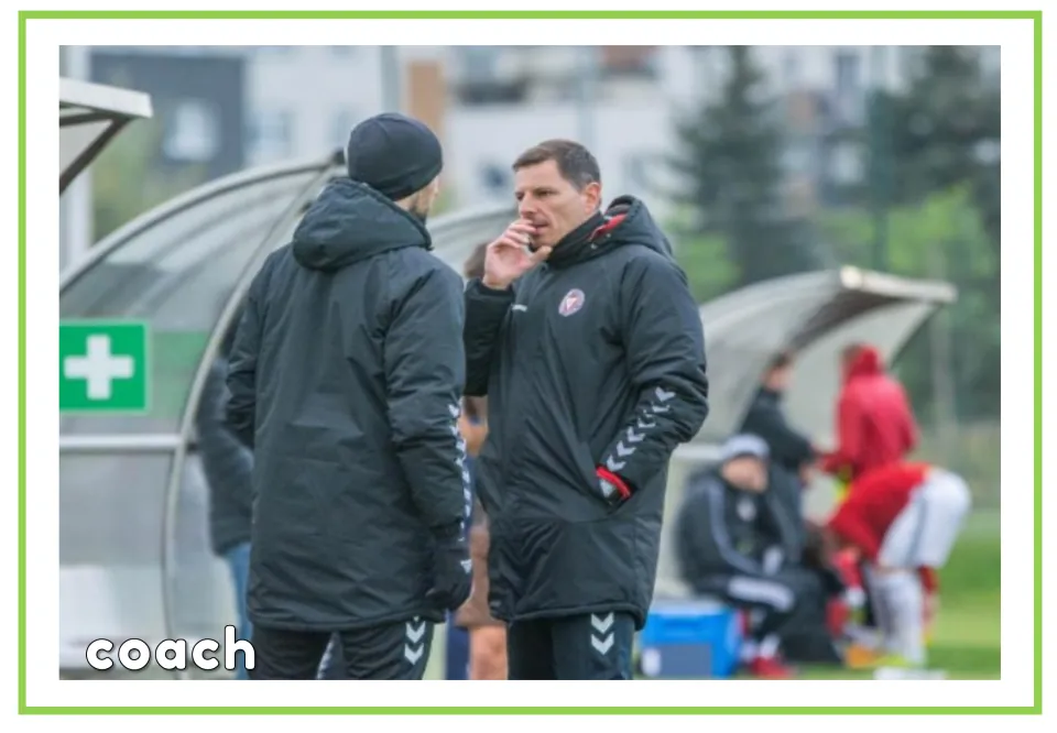 Labeled soccer vocabulary flashcard showing the word coach and two adults talking beside the team benches