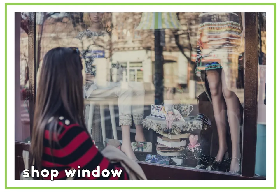 Labeled shopping vocabulary flashcard for 'shop window,' showing a shopper viewing a clothing display