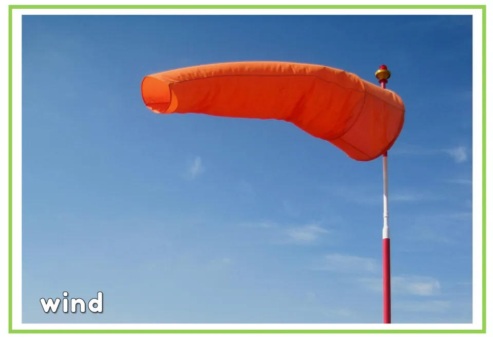 Labeled weather vocabulary flashcard showing an orange windsock against the sky with the English word 'wind'