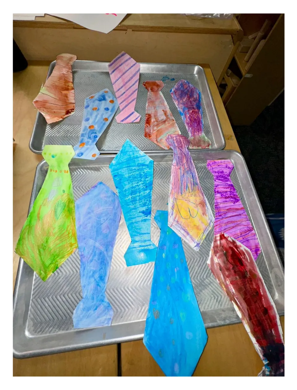 Second student example sheet for the tie craft, showing painted paper ties on trays with crayon designs
