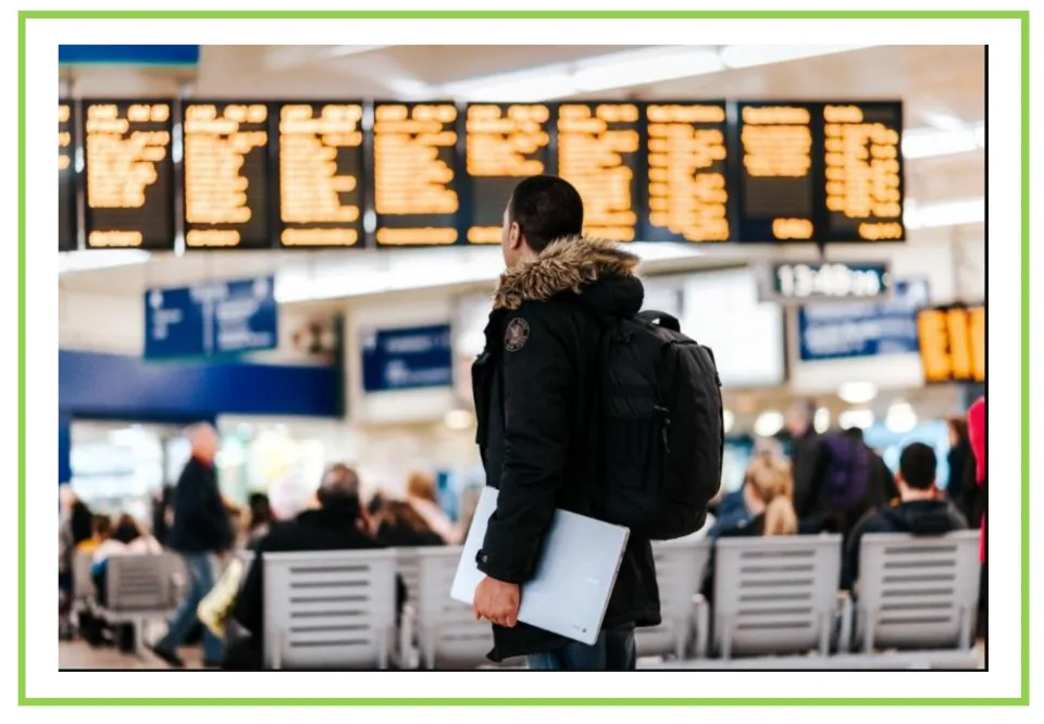 Airport vocabulary flashcard without a label, showing a traveler wearing a backpack below flight information boards