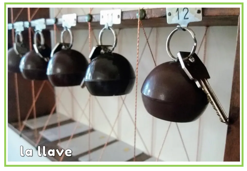 Spanish hotel vocabulary flashcard labeled 'la llave' (key), showing room keys hanging from numbered hooks