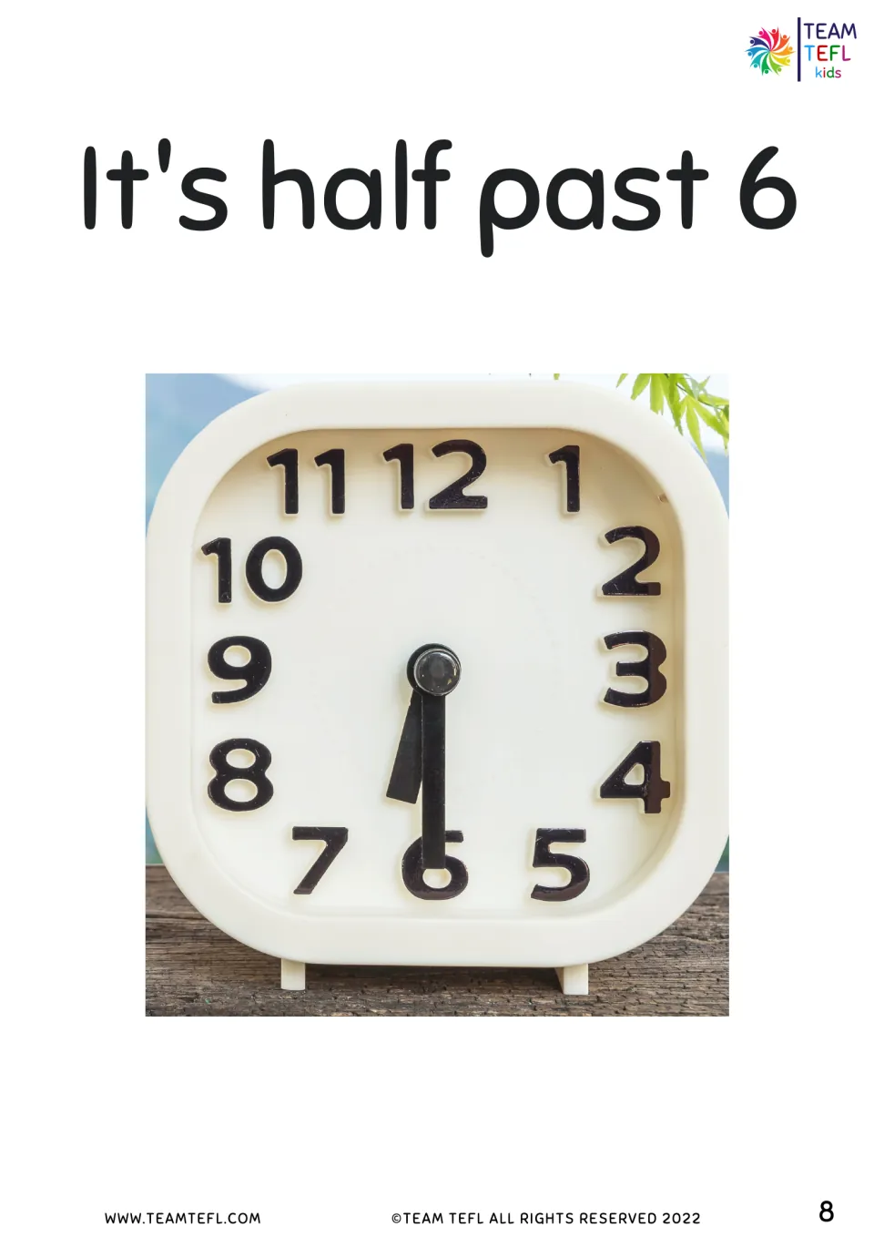 It's half past 6 flashcard: photo of a white desk clock with both hands pointing down toward the 6