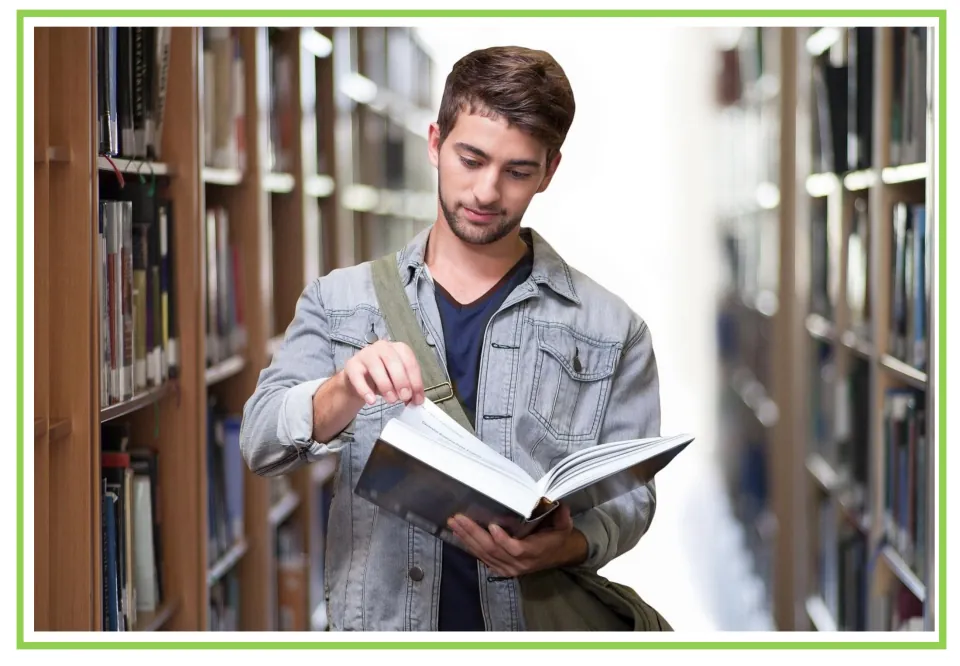 University library flashcard: a young man in a denim jacket reads an open book between shelves, a picture to talk about