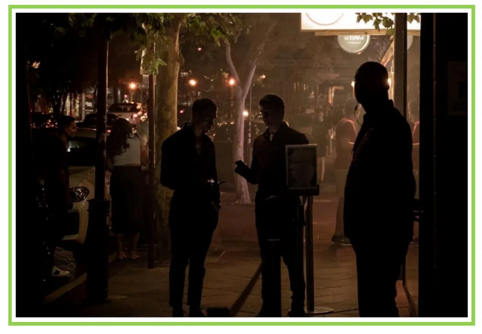 Bar and club discussion flashcard 2: people standing near an entrance on a city sidewalk after dark