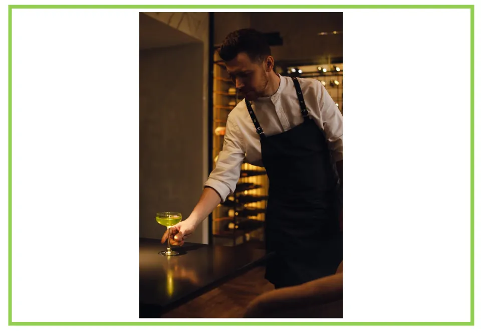Bar and club discussion flashcard 3: a server wearing a black apron places a green drink on a table