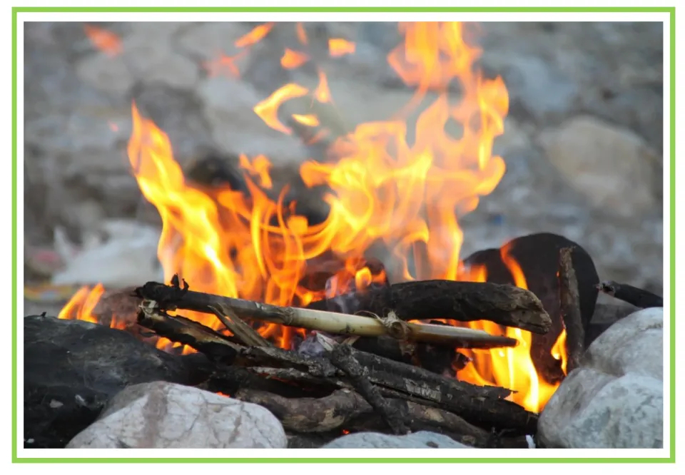 Camping writing and discussion prompt card 6: bright flames rising from logs in a campfire surrounded by rocks