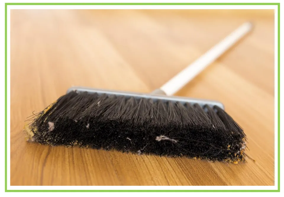 Cleaning discussion flashcard showing a long-handled broom with dust caught in its dark bristles on a wood floor