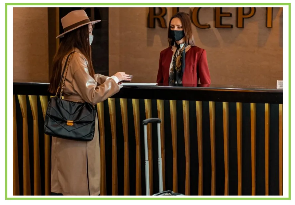 Hotel writing and discussion flashcard 8: a guest with luggage faces a receptionist; both wear masks
