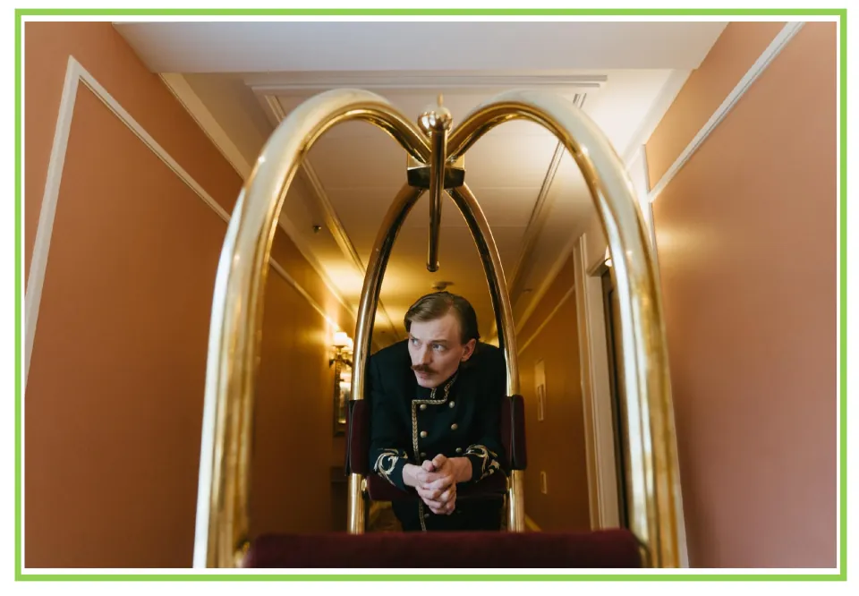 Hotel writing and discussion flashcard 10: a uniformed bellhop leans on a luggage cart in a hallway