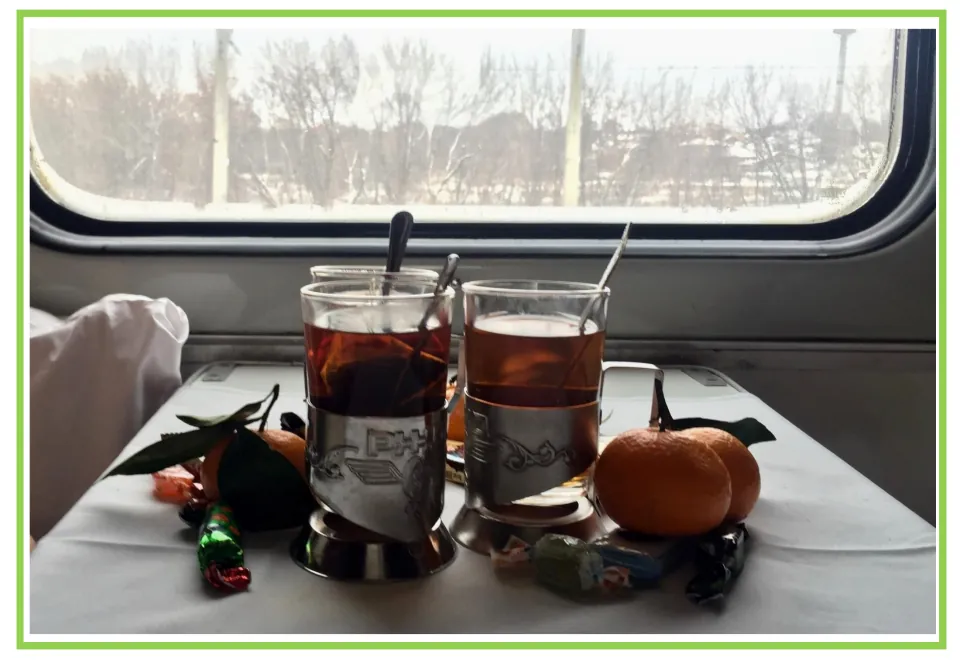 Train writing and discussion prompt card 7: glasses of tea, oranges, and candy on a table by a train window